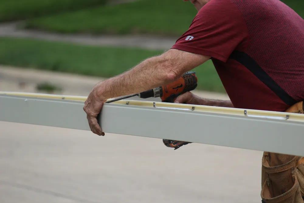 Male contractor using a Seamless Gutter Machine to prepare seamless gutter to be installed on a residential building